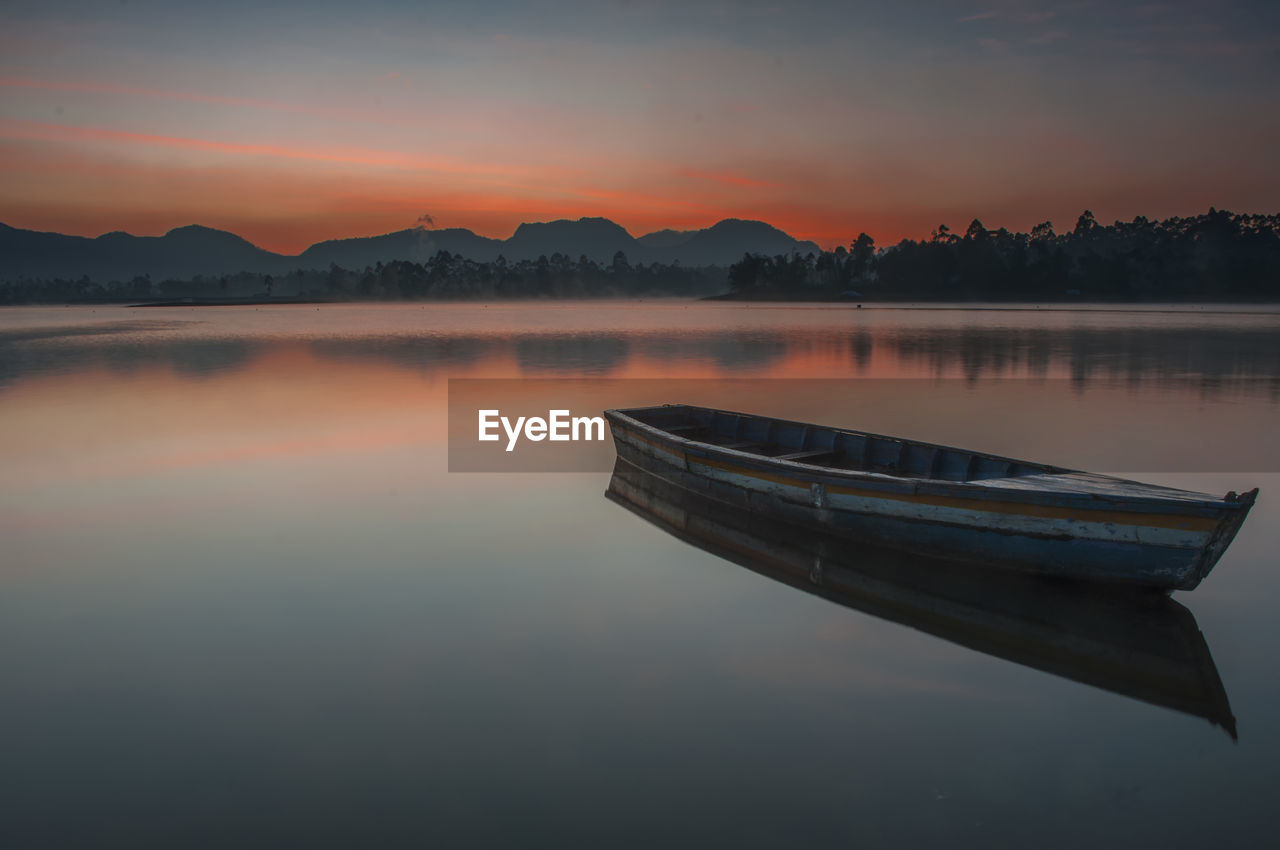 Boat moored in lake against sky during sunset