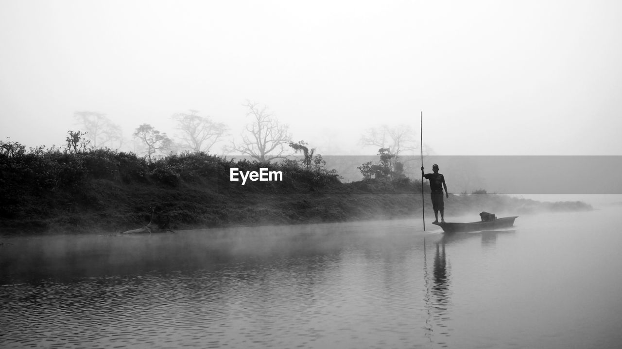 Man holding pole while standing on boat in river during foggy weather