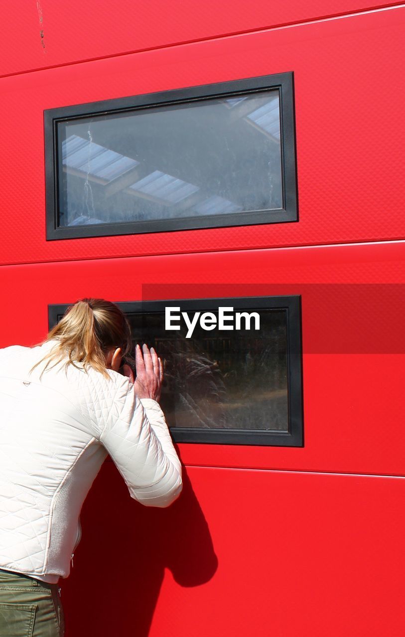 REAR VIEW OF WOMAN STANDING BY RED WALL