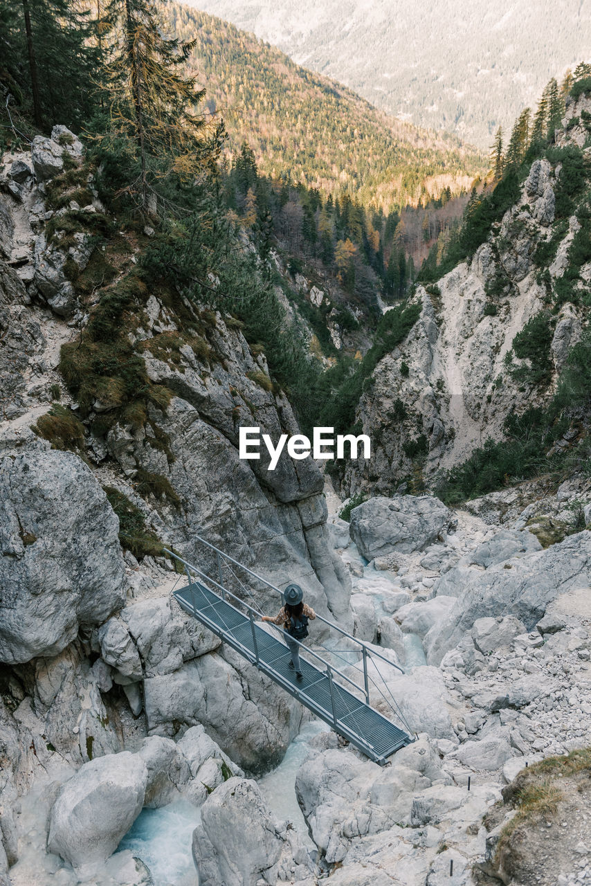 Woman standing on footbridge over mountain torrent, looking at landscape view