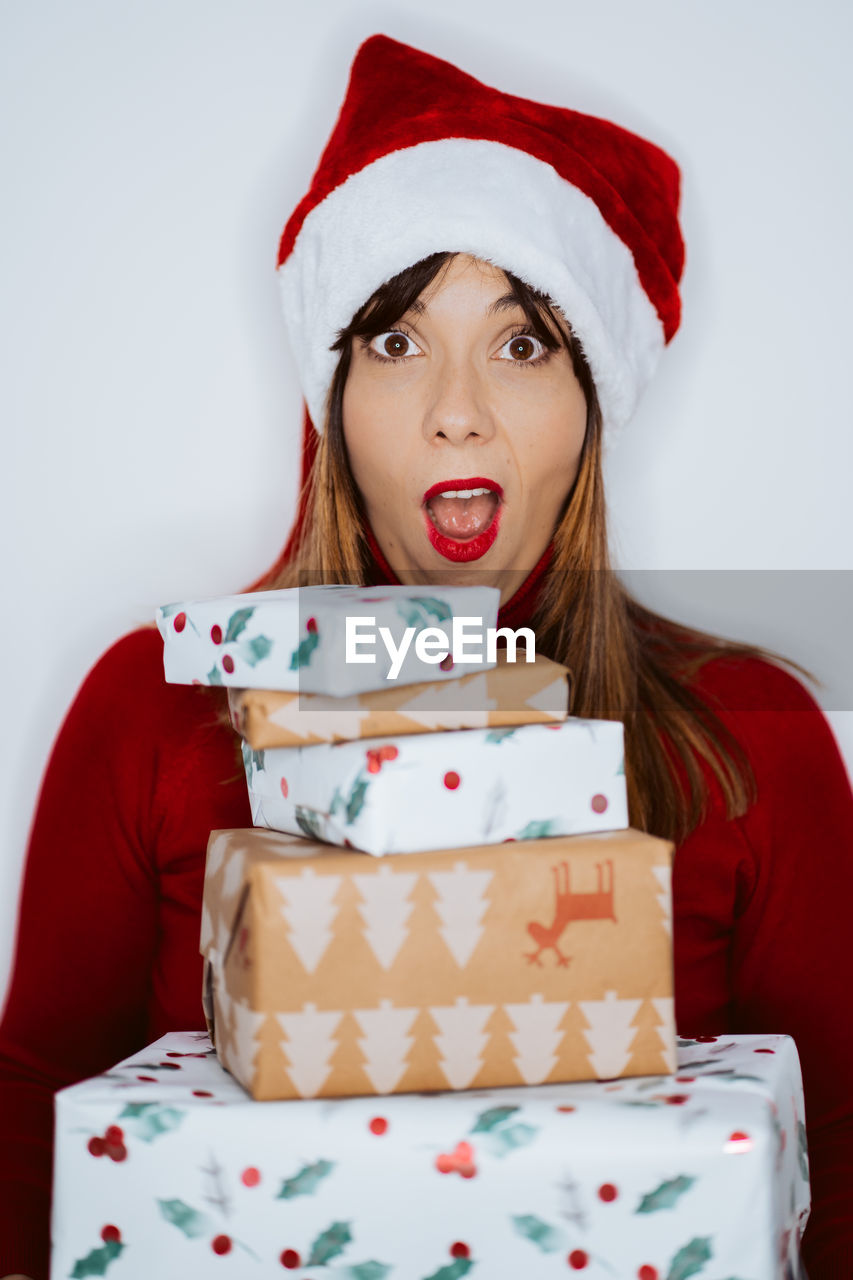 Portrait of smiling woman holding christmas gifts while standing against white background