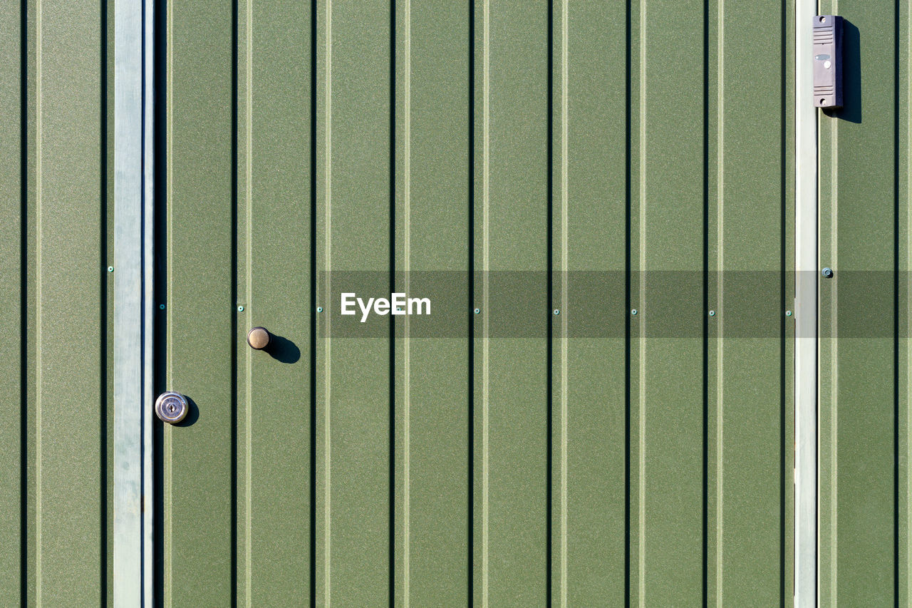 Green metal fence and doors made of corrugated steel sheet  and a surveillance camera.