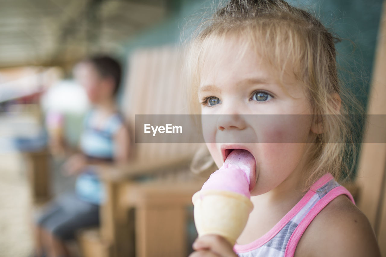 Young cute girl happily licking pink ice cream on summer day.