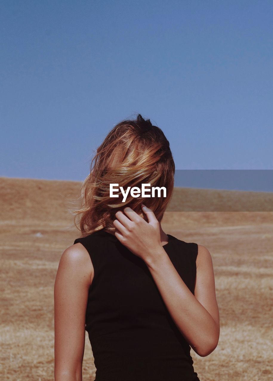 Woman covering face at beach against clear sky