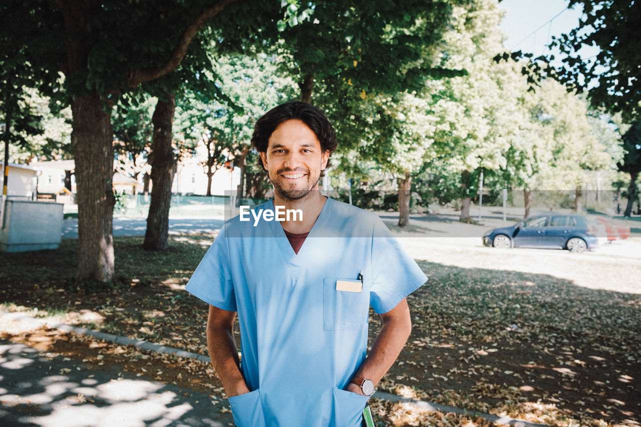 Portrait of smiling male nurse standing with hands in pockets at nursing home