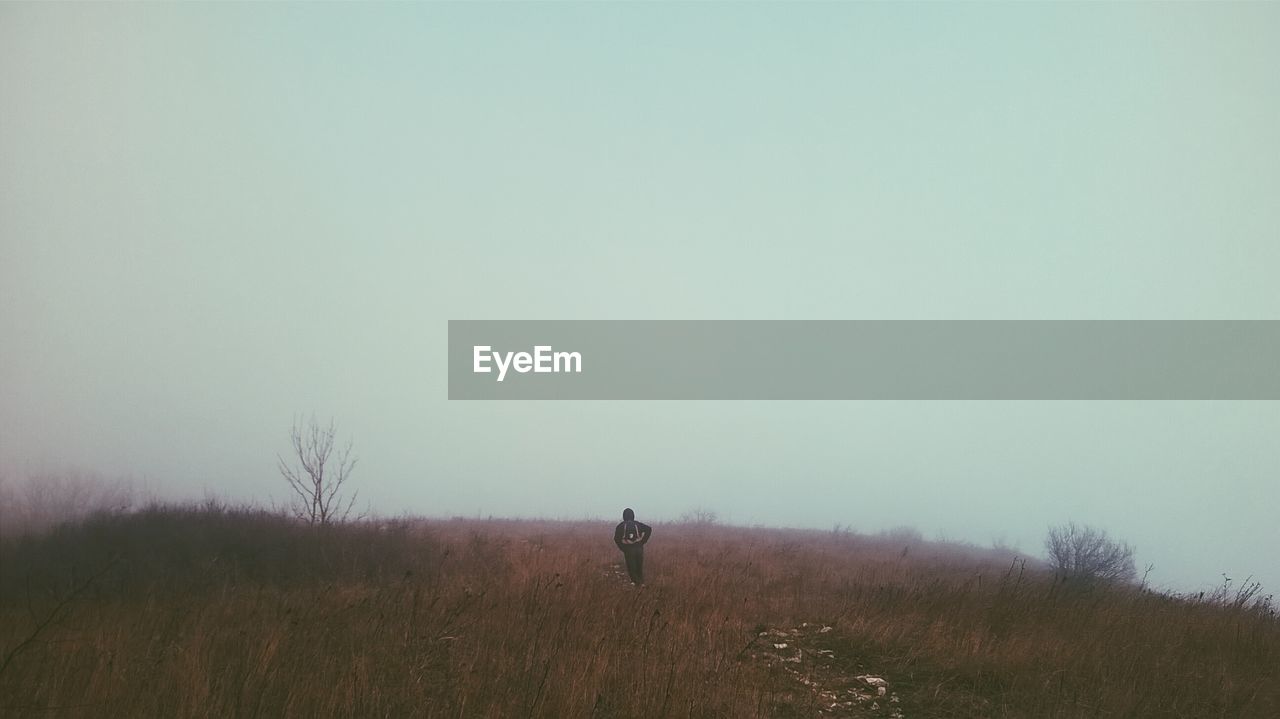 Hiker on grassy field against clear sky