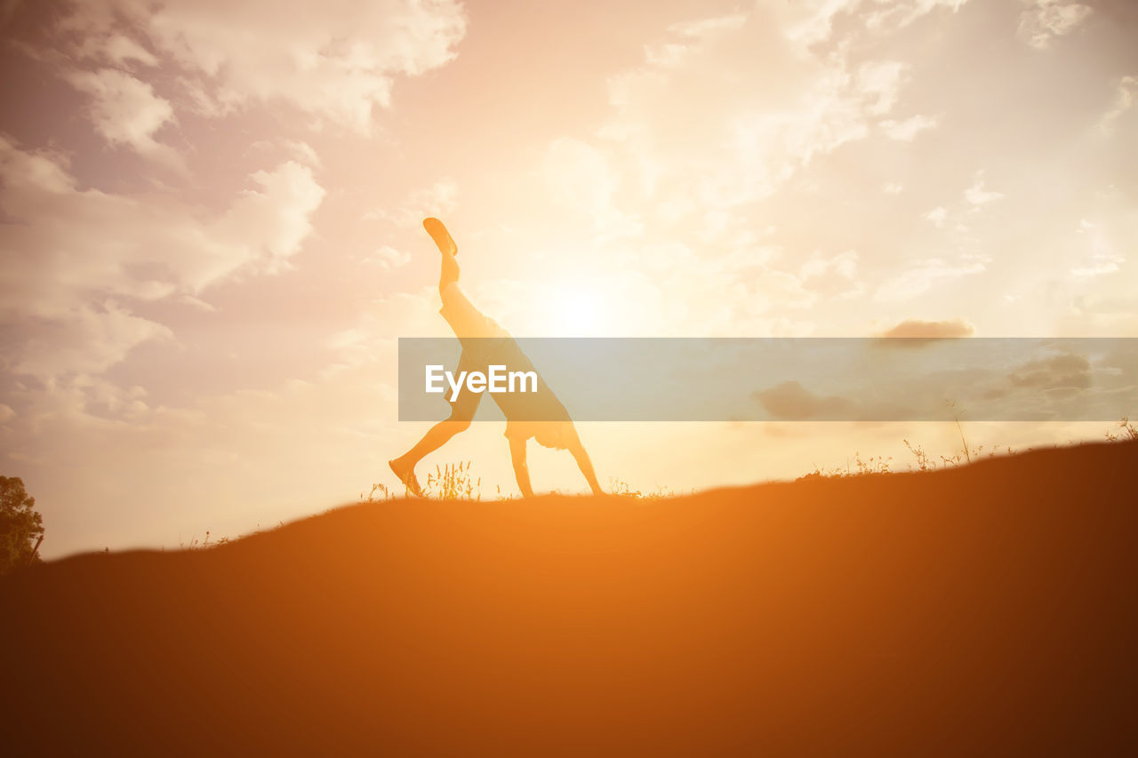 Silhouette man doing handstand on field against sky during sunset