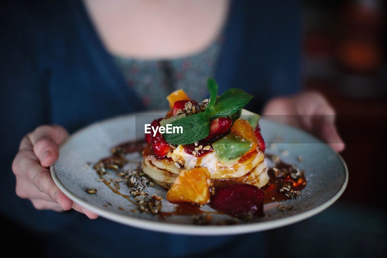 Midsection of woman holding pancake in plate