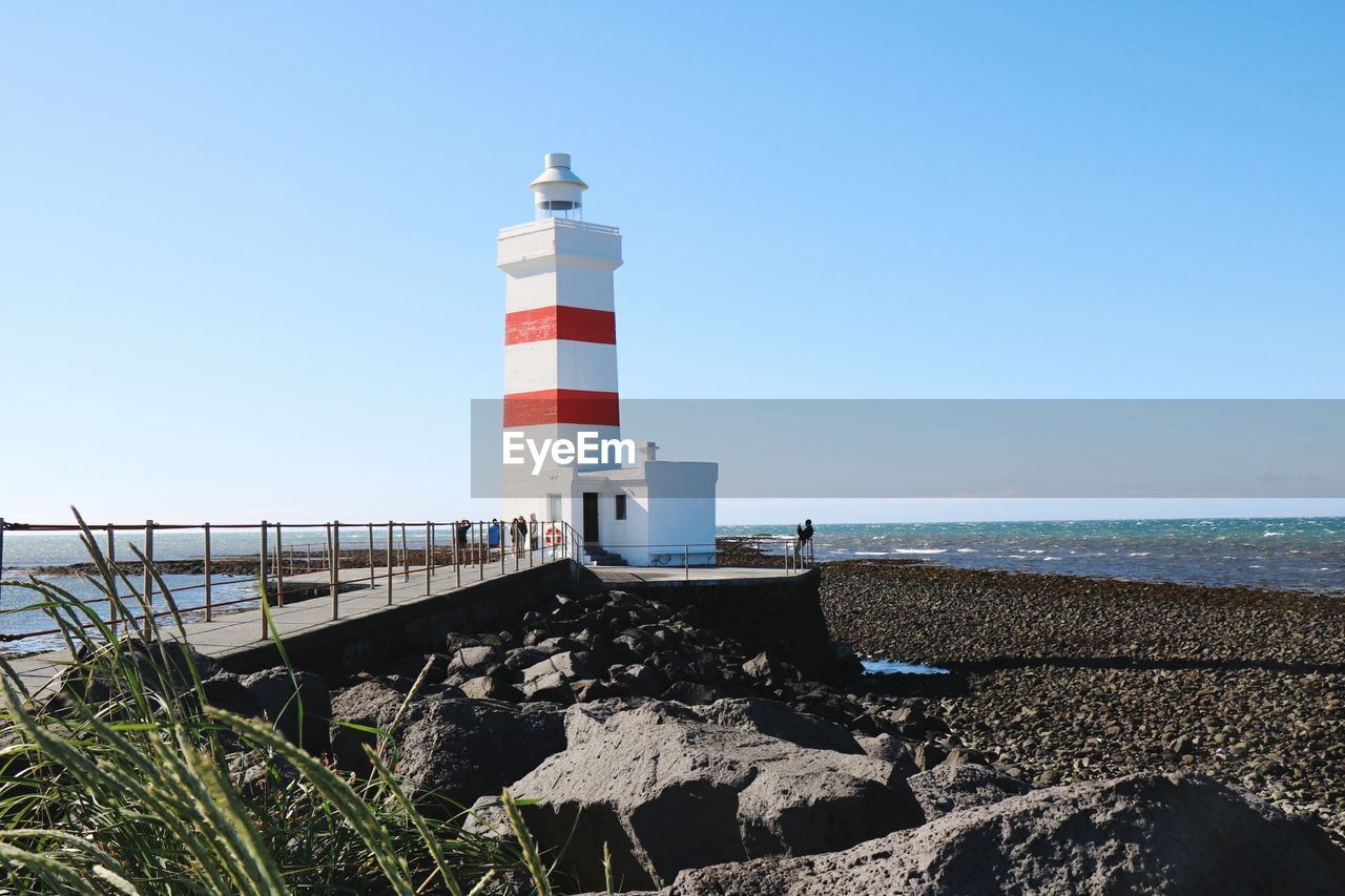 Lighthouse by sea against clear sky