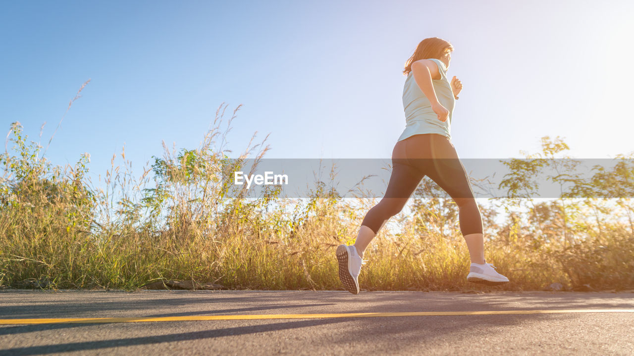 Full length of woman running on road against sky