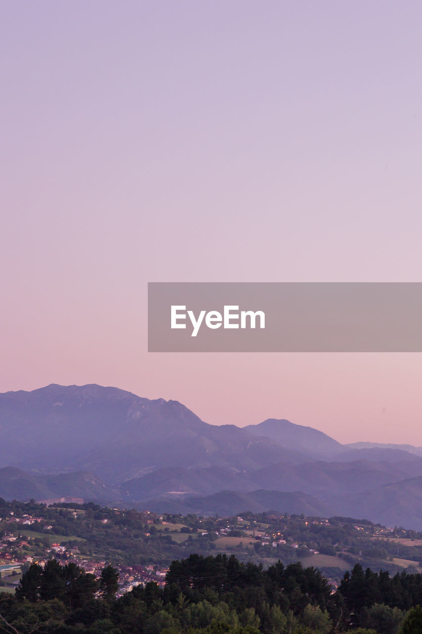 mountain, landscape, environment, sky, horizon, scenics - nature, nature, beauty in nature, dawn, sunset, pink, city, architecture, mountain range, land, no people, copy space, tranquility, outdoors, tree, purple, plant, building, travel, clear sky, travel destinations, building exterior, twilight, tranquil scene, evening, built structure, sun, high angle view, cityscape, idyllic, cloud, magenta