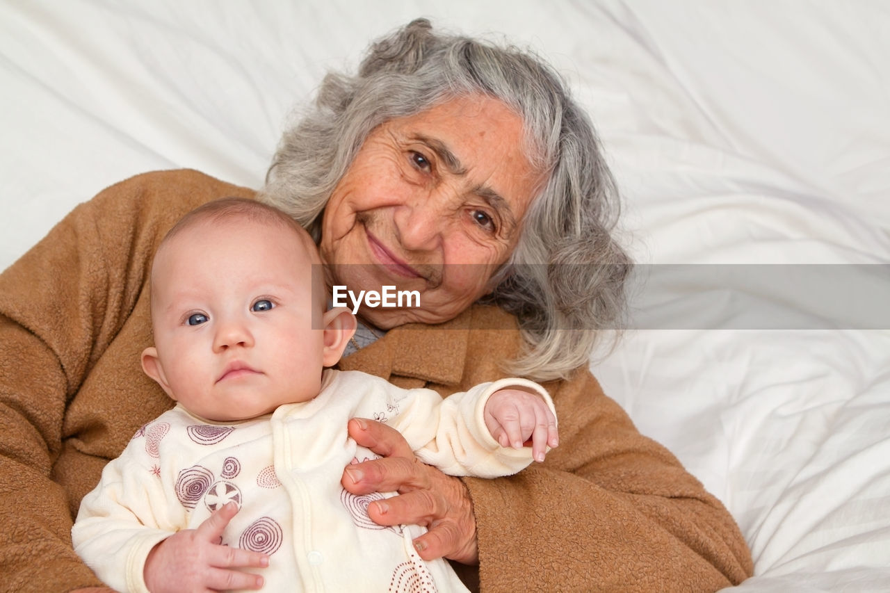 Portrait of grandmother with baby girl lying on bed at home