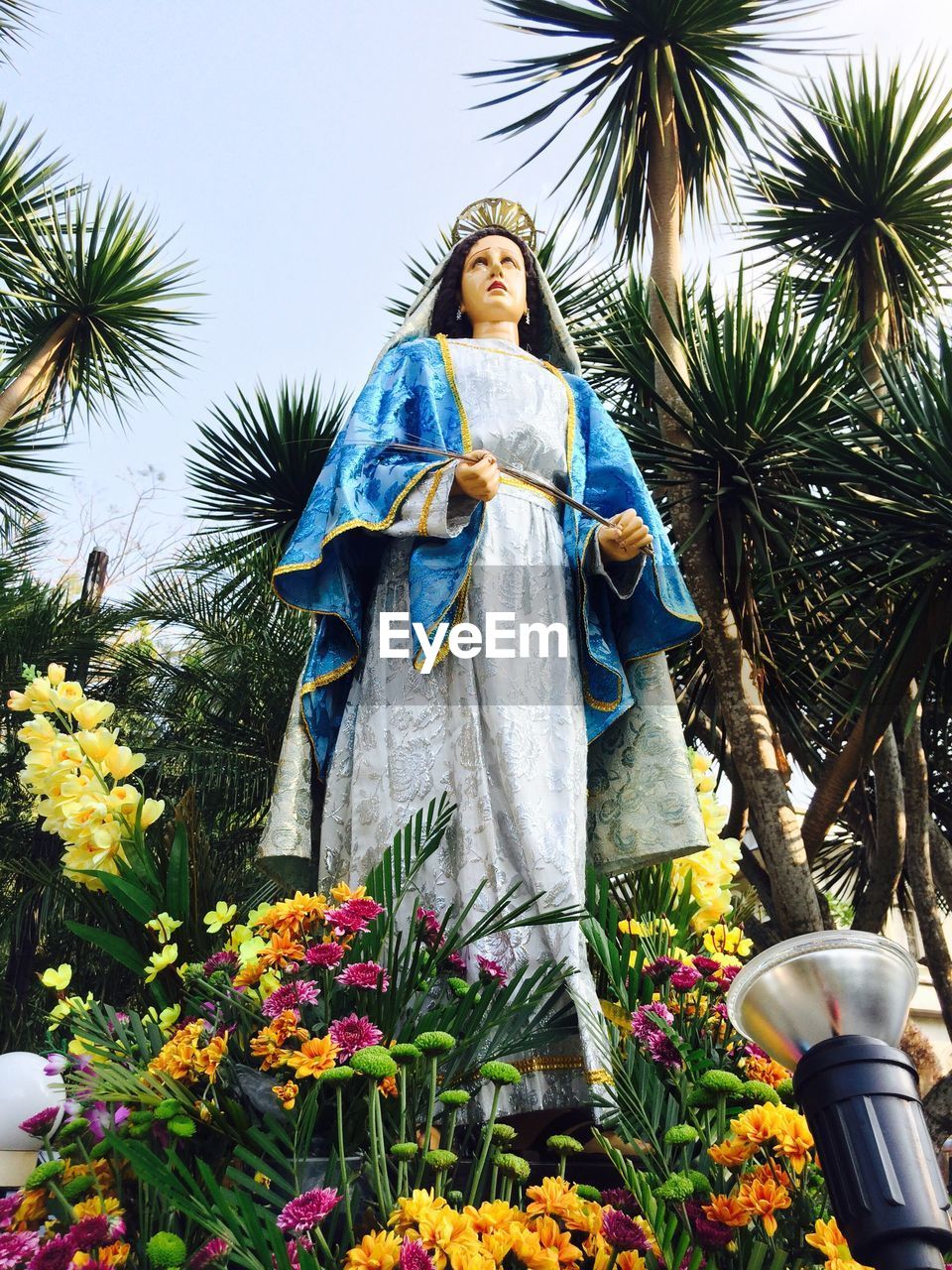 Bouquets around virgin mary statue against trees outside church