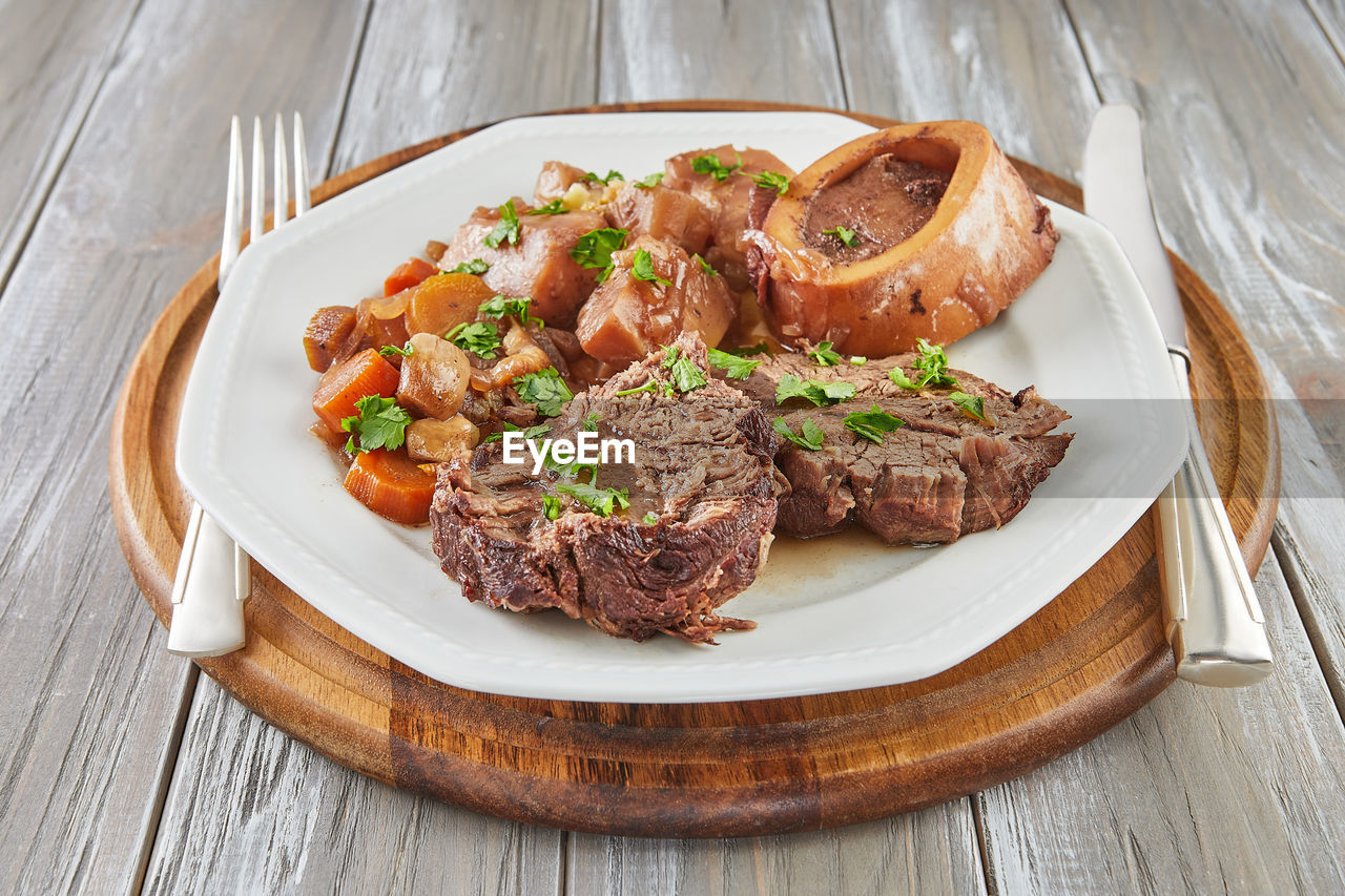 Ossobuco with vegetables on plate with knife and fork on wooden background