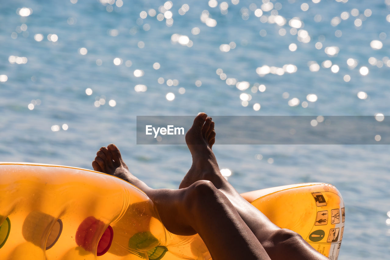 Low section of woman lying on inflatable raft by sea during sunny day