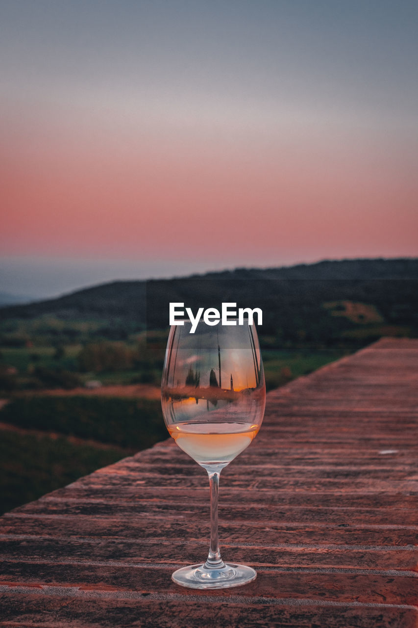 Wineglass on table against sky during sunset