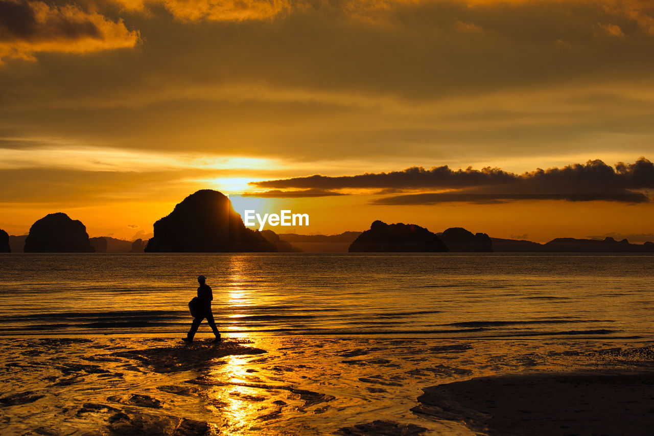 SILHOUETTE MAN ON SHORE AGAINST SKY DURING SUNSET