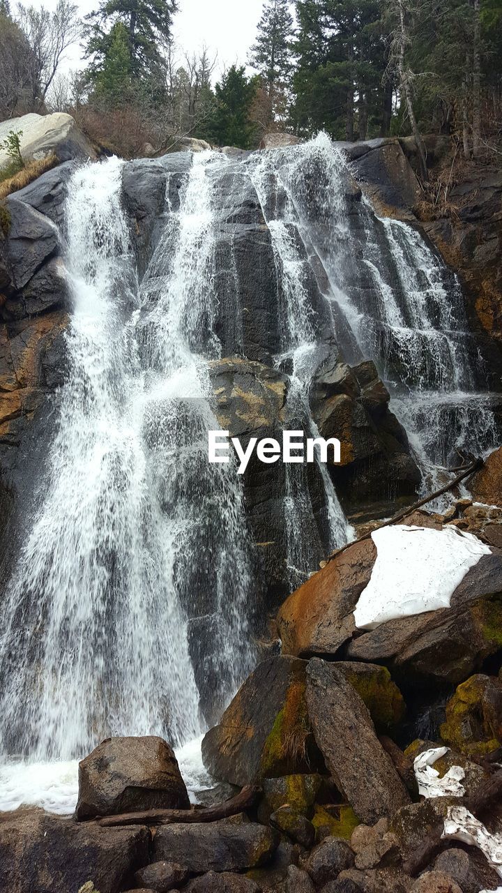 LOW ANGLE VIEW OF WATERFALL AGAINST TREES