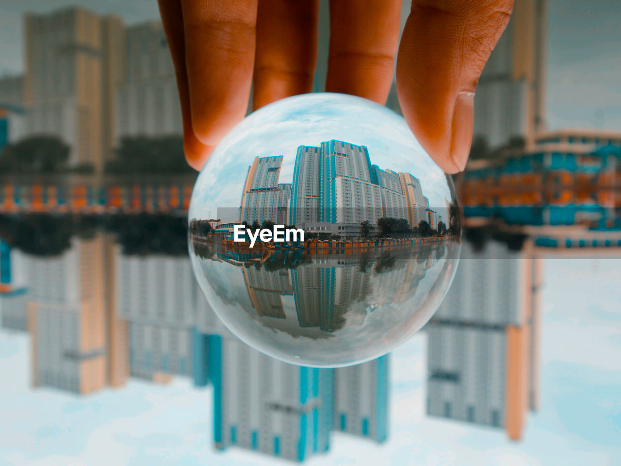 architecture, building exterior, reflection, sphere, built structure, water, city, blue, focus on foreground, nature, close-up, travel destinations, glass, world, building, one person, outdoors, hand, travel, day, holding, sky, crystal ball