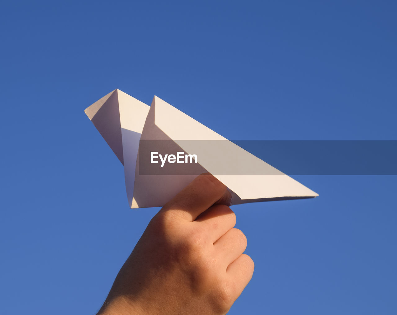 LOW ANGLE VIEW OF HAND HOLDING PAPER AGAINST BLUE SKY