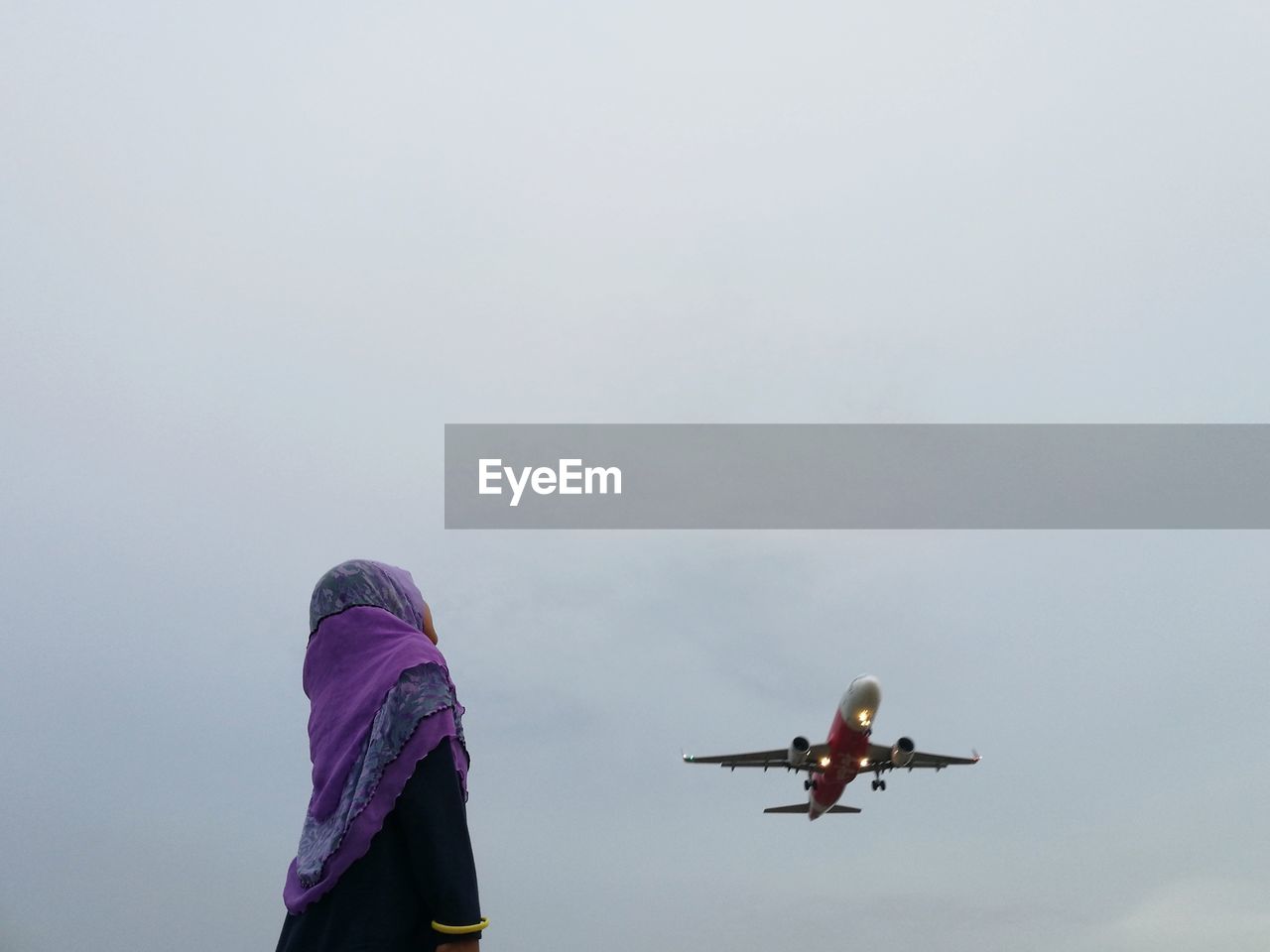 Girl in traditional clothing looking at airplane flying against sky