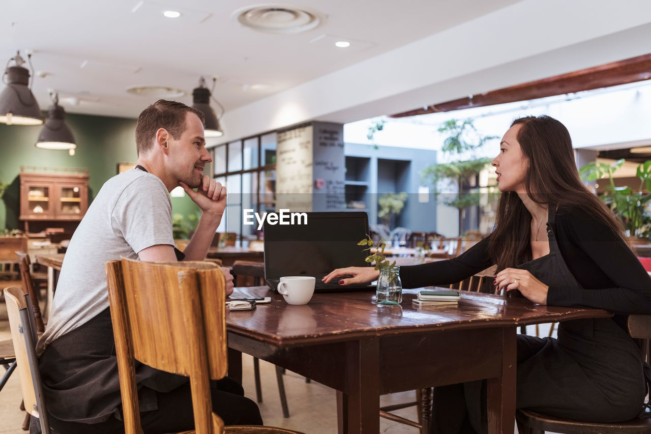 Male and female partners using laptop at table in cafe