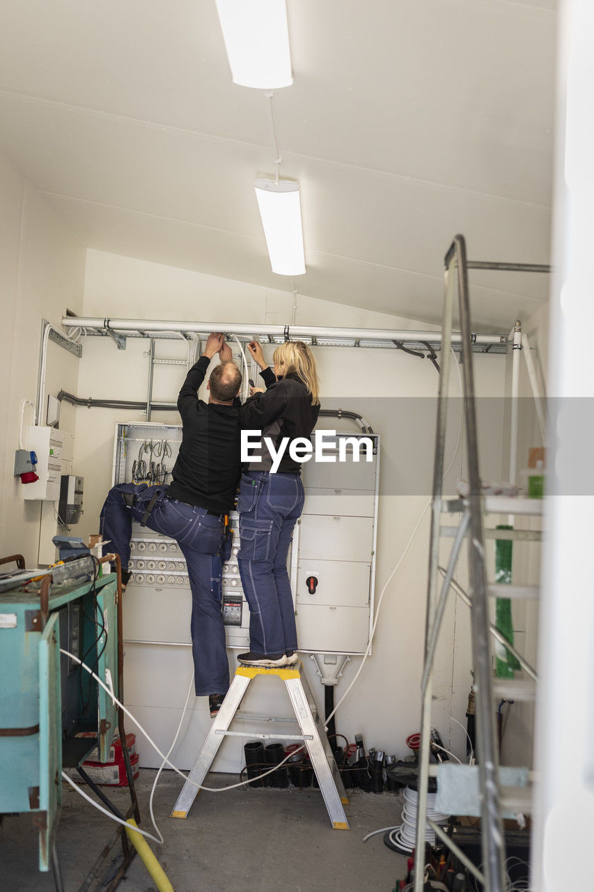 Male and female electrician fixing cables in meter room at industry