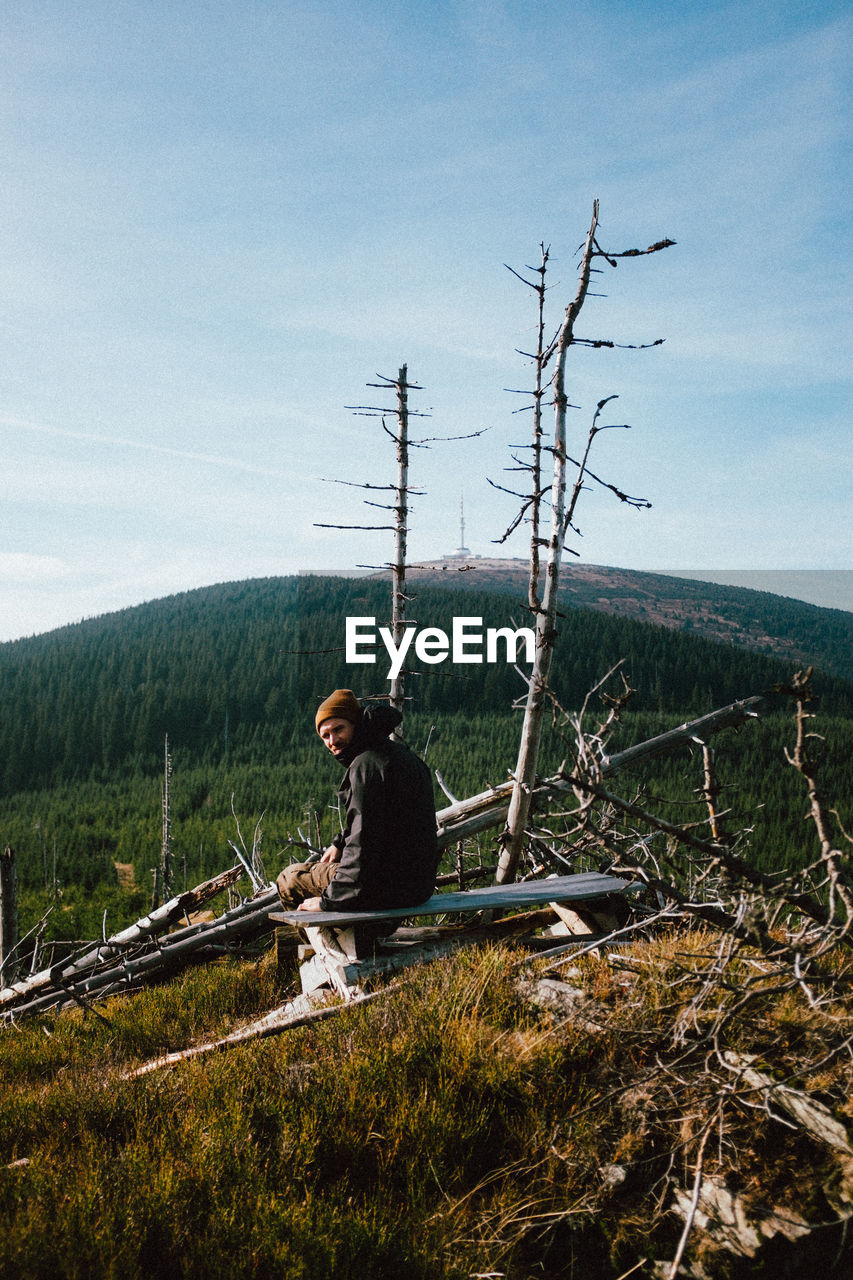 Portrait of man sitting against trees in sunny day