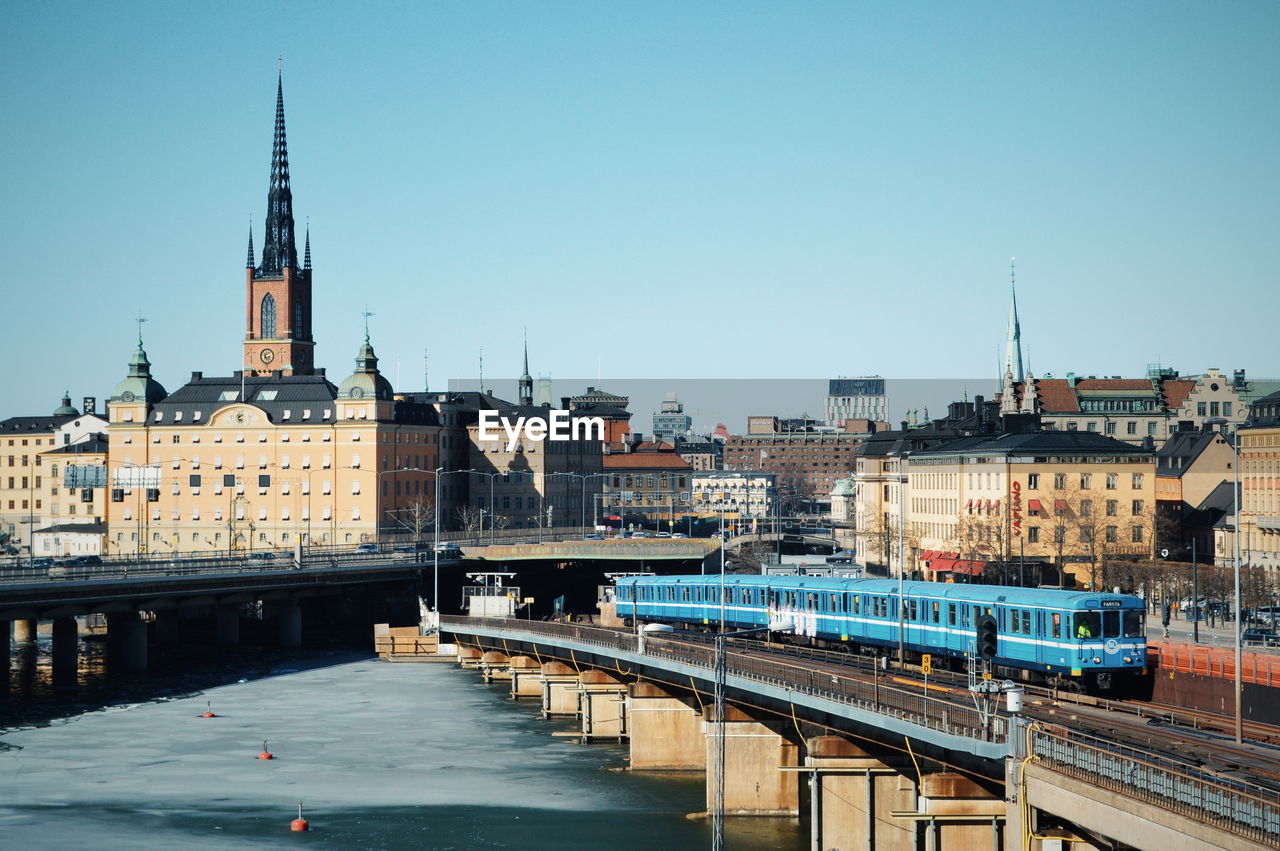 BRIDGE OVER RIVER AMIDST BUILDINGS IN CITY AGAINST SKY