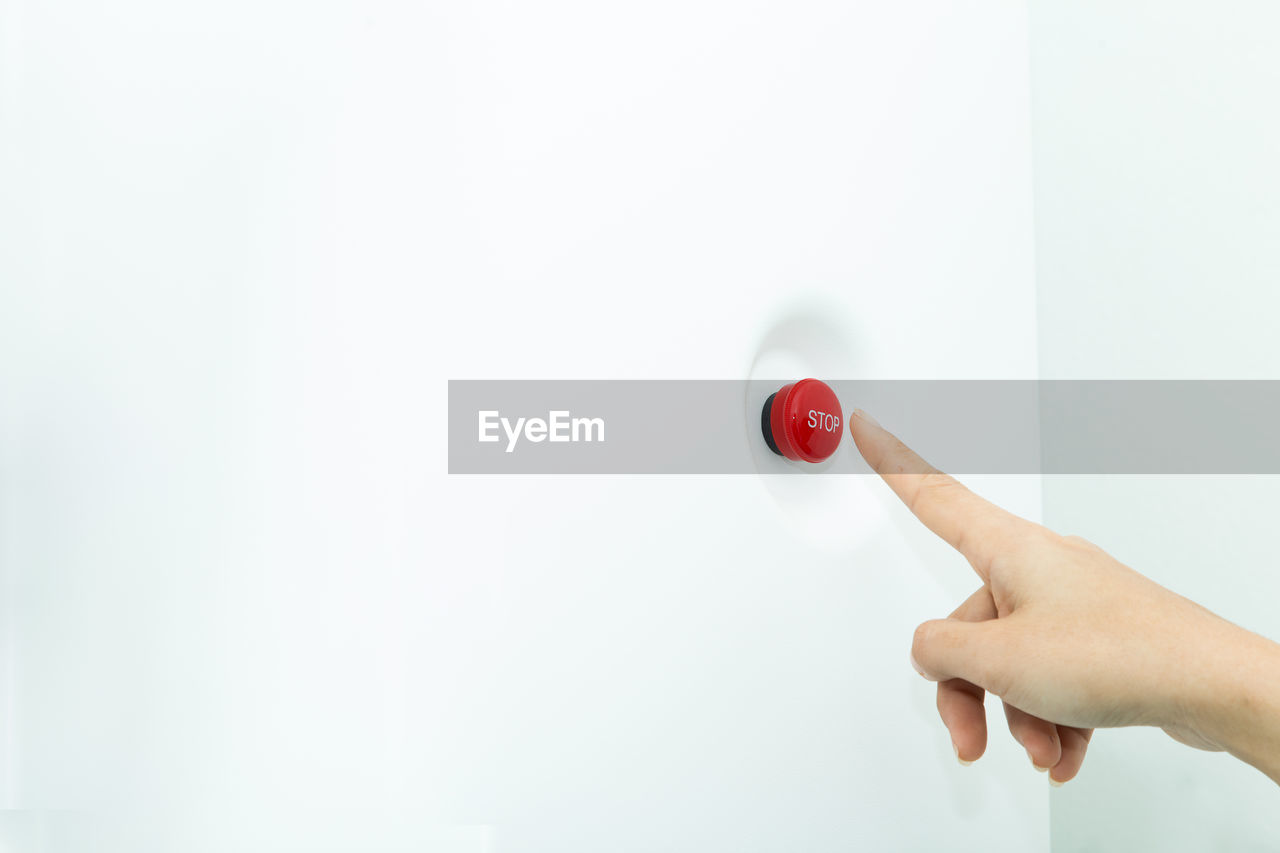 Close-up of hand pressing red button on wall