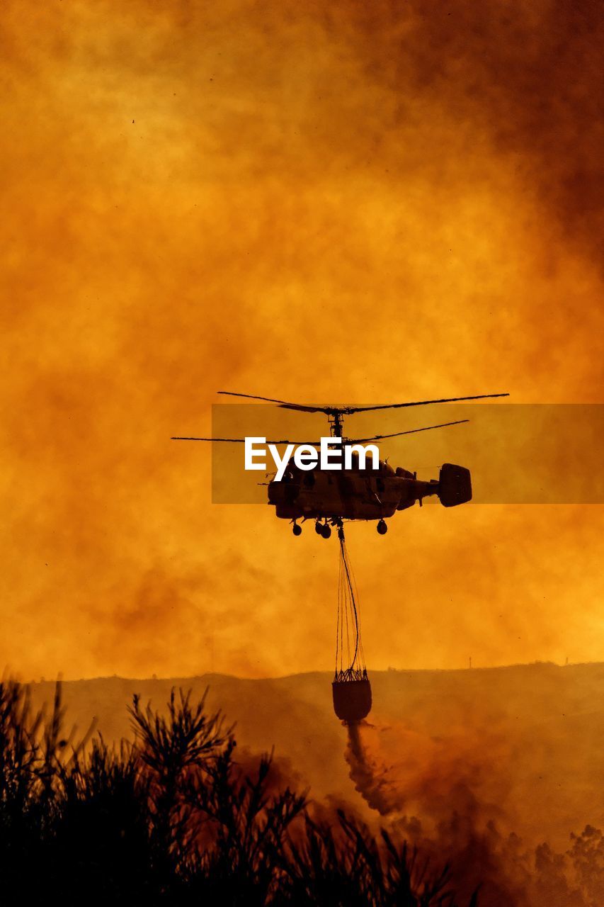 Silhouette helicopter against orange sky