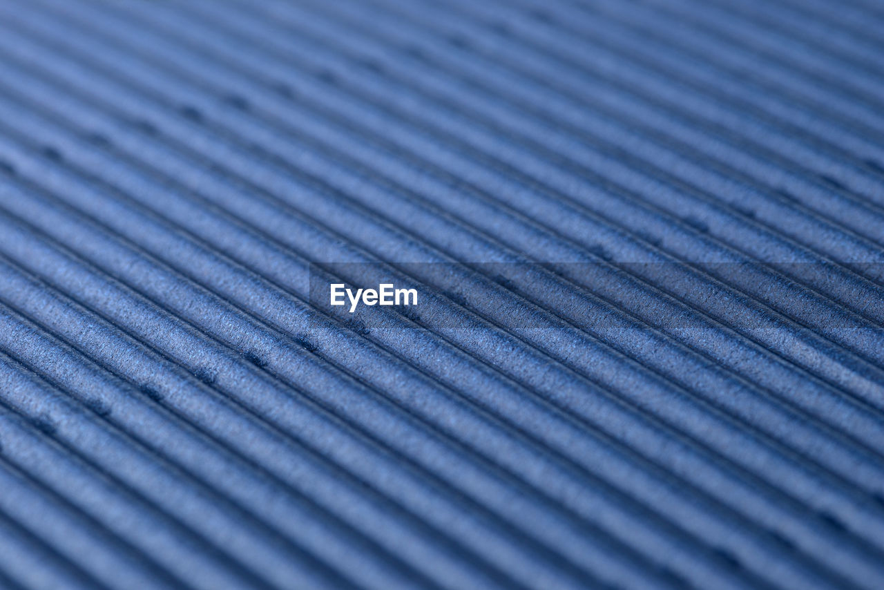 Background made of blue corrugated cardboard with diagonal stripes, shallow depth of field.