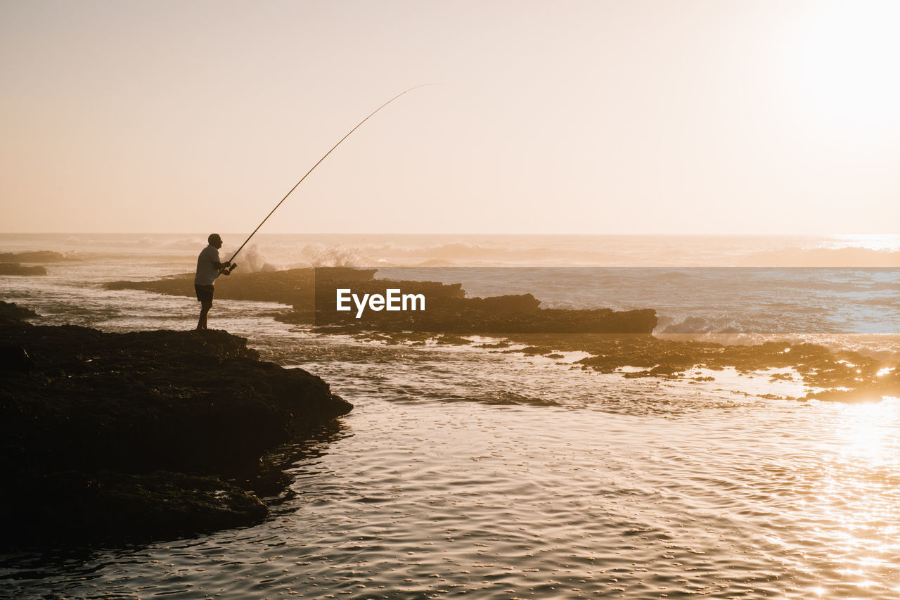 Man fishing in sea against sky