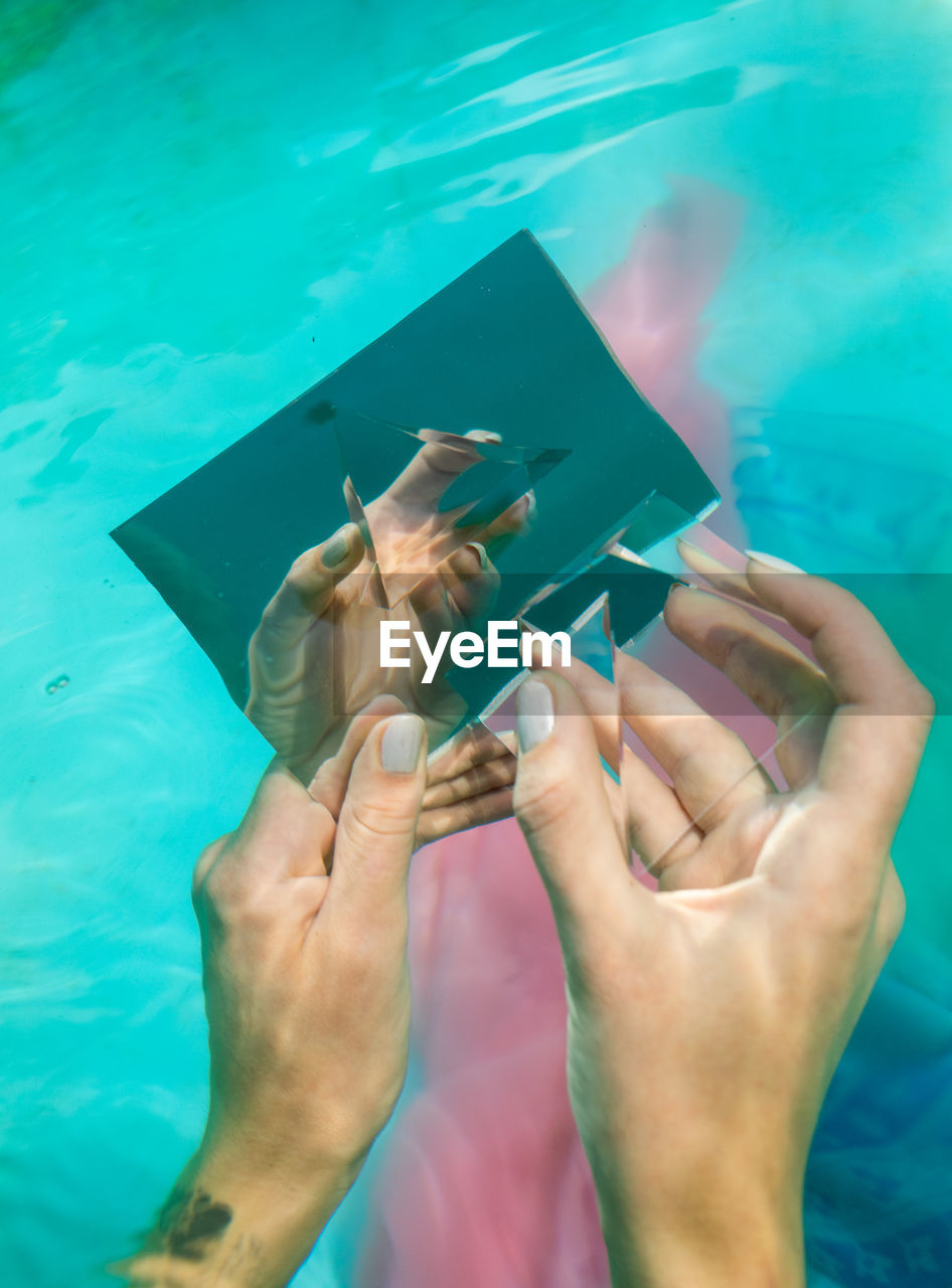 Cropped hands of woman holding mirror and prism in swimming pool