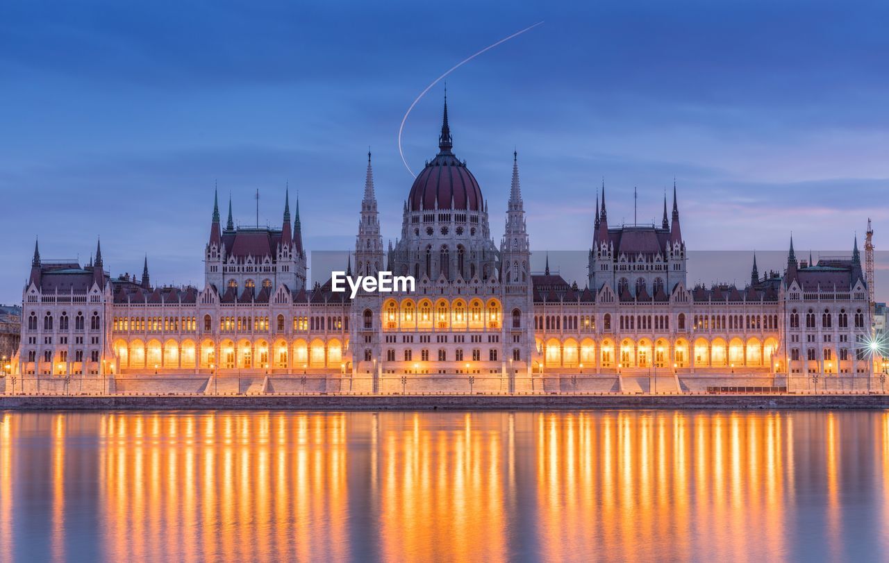 Hungarian parliament building by river in city at dusk