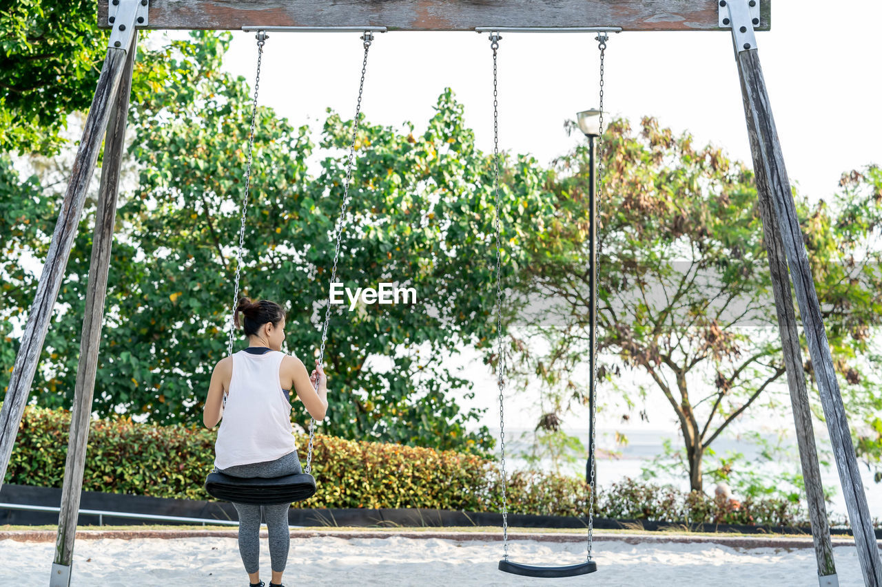 REAR VIEW OF WOMAN STANDING AGAINST PLANTS