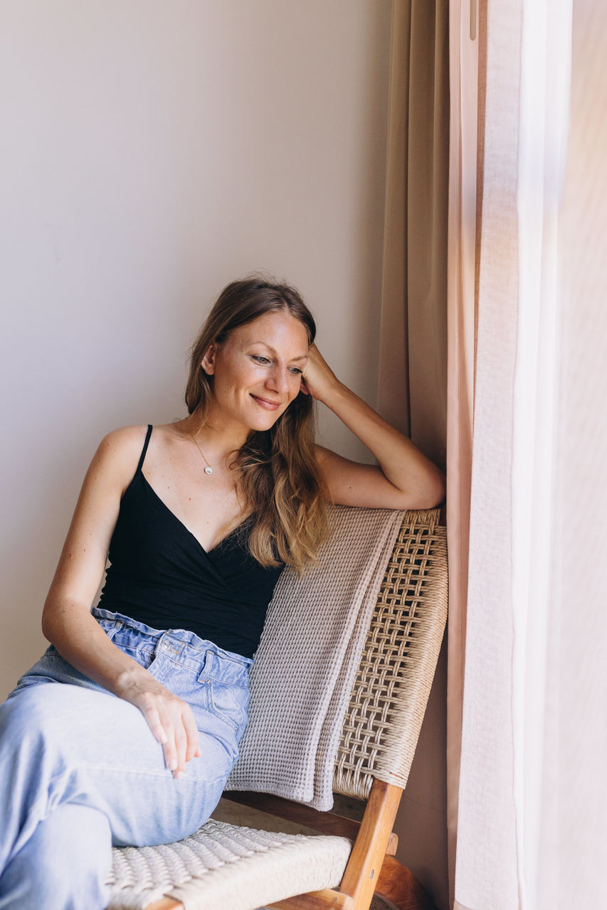 Portrait of young woman looking down sitting on a chair cross legged