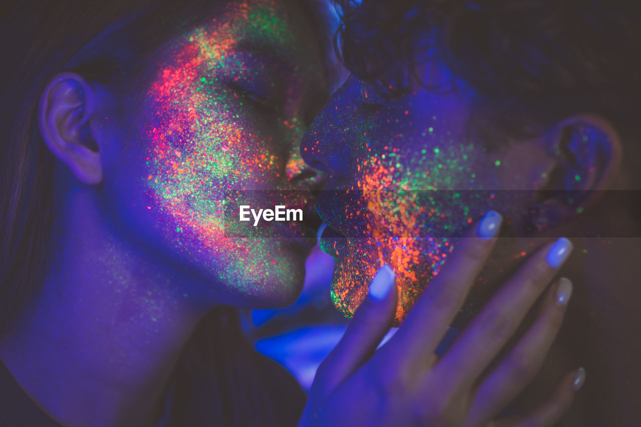 Close-up of couple with multi colored face paint kissing