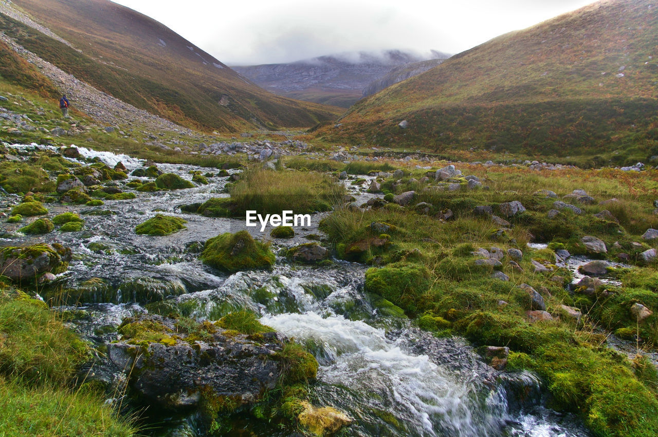 Scenic view of stream by mountains against sky