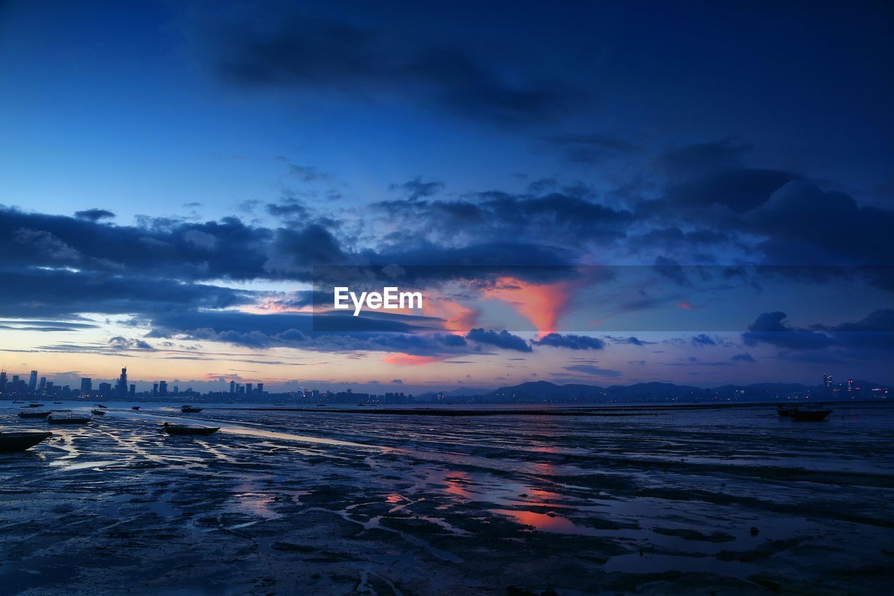 River by city against cloudy sky during sunset