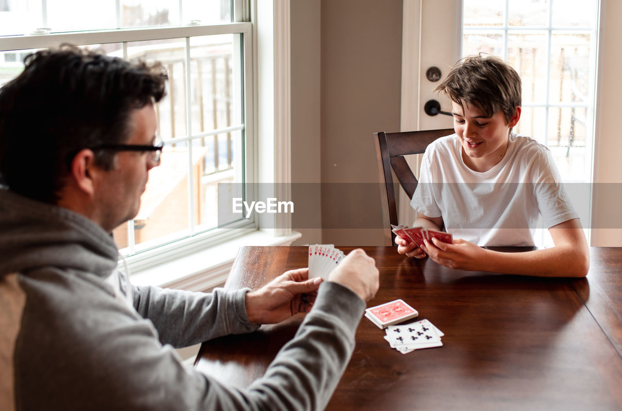 Adolescent boy and his father playing cards at the table together.