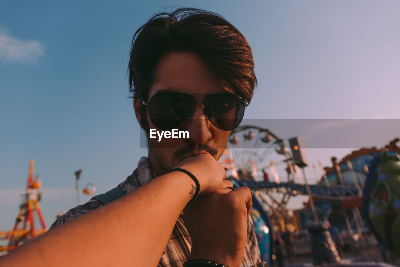 Man kissing girlfriend hand at amusement park against sky