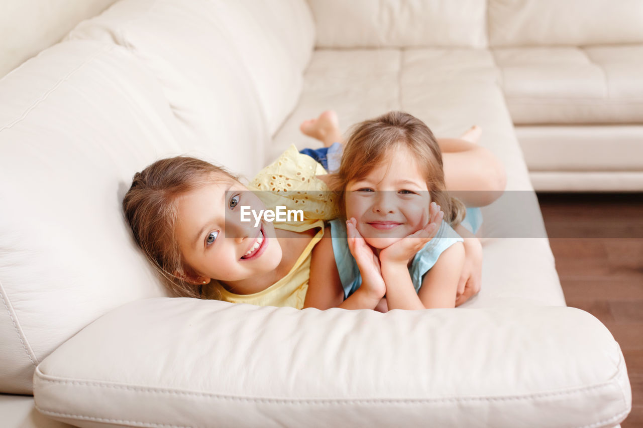 Two cute little caucasian girls siblings playing at home. adorable children kids lying on couch