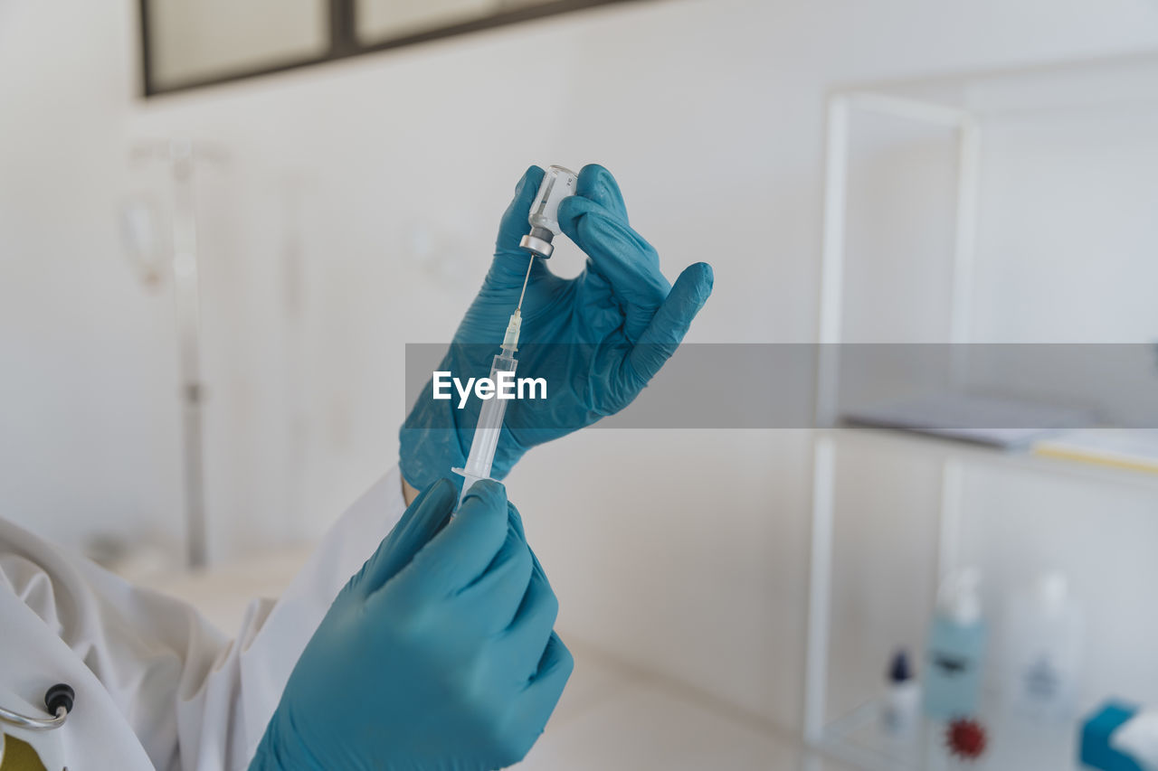 Close-up of doctor filling syringe with covid-19 vaccine at examination room