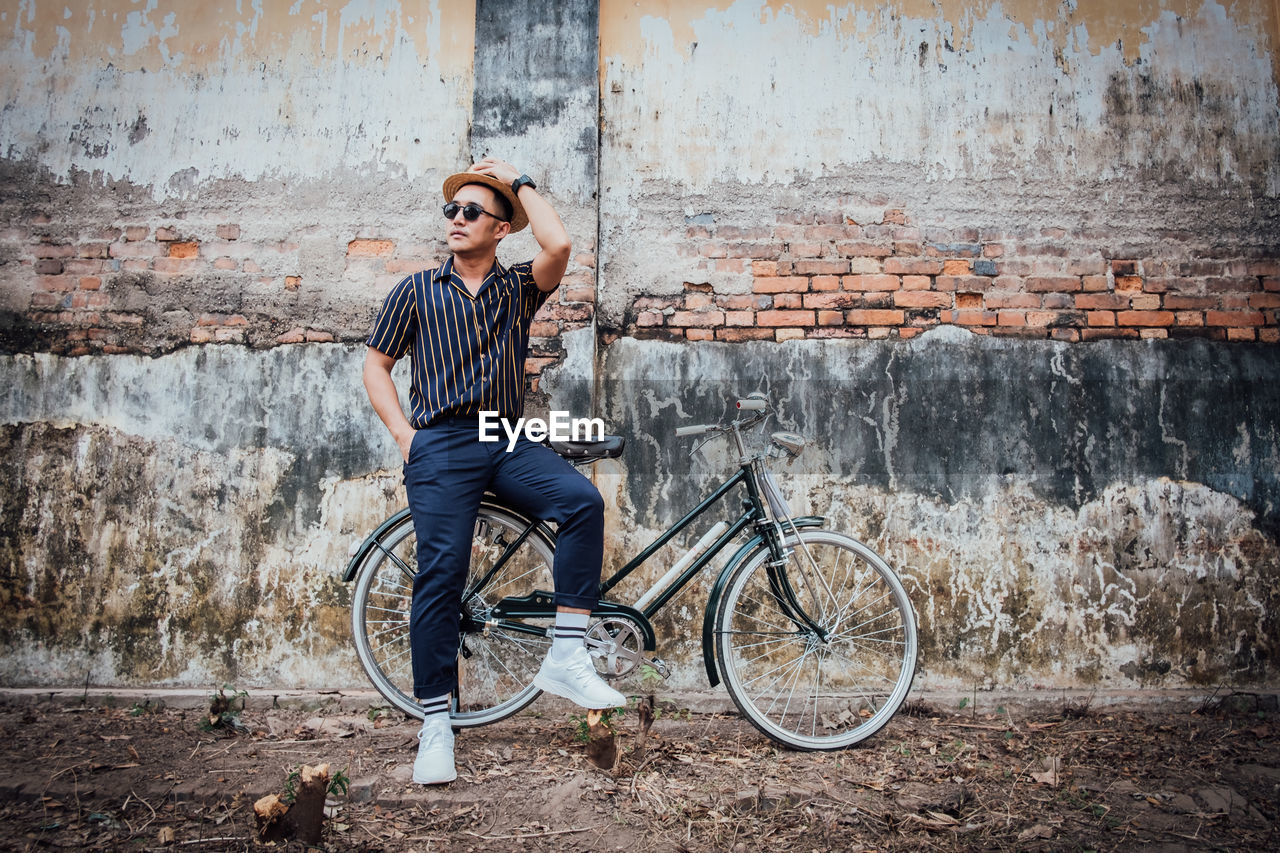 Man sitting on bicycle against wall in city