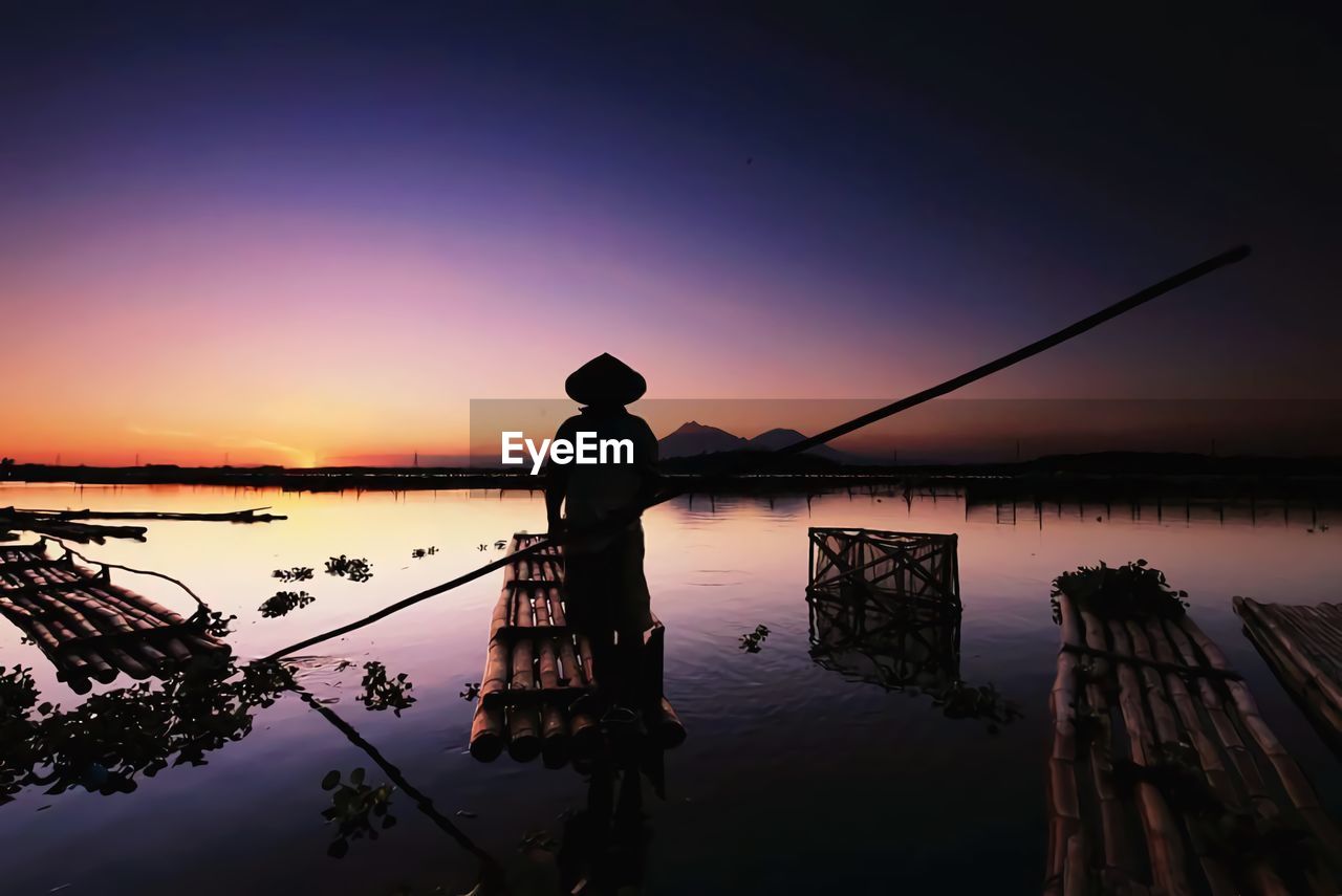 Silhouette man fishing in lake against sky during sunset