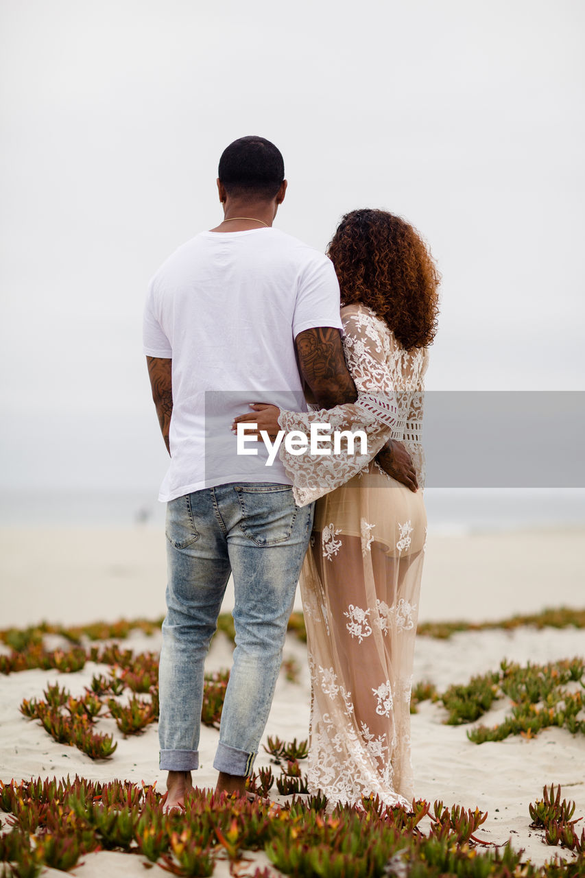 Mixed race couple embracing on sand dunes maternity