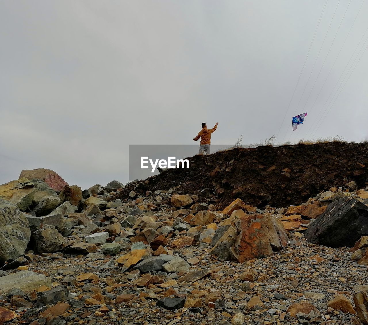 Low angle view of man with kite on rock against sky