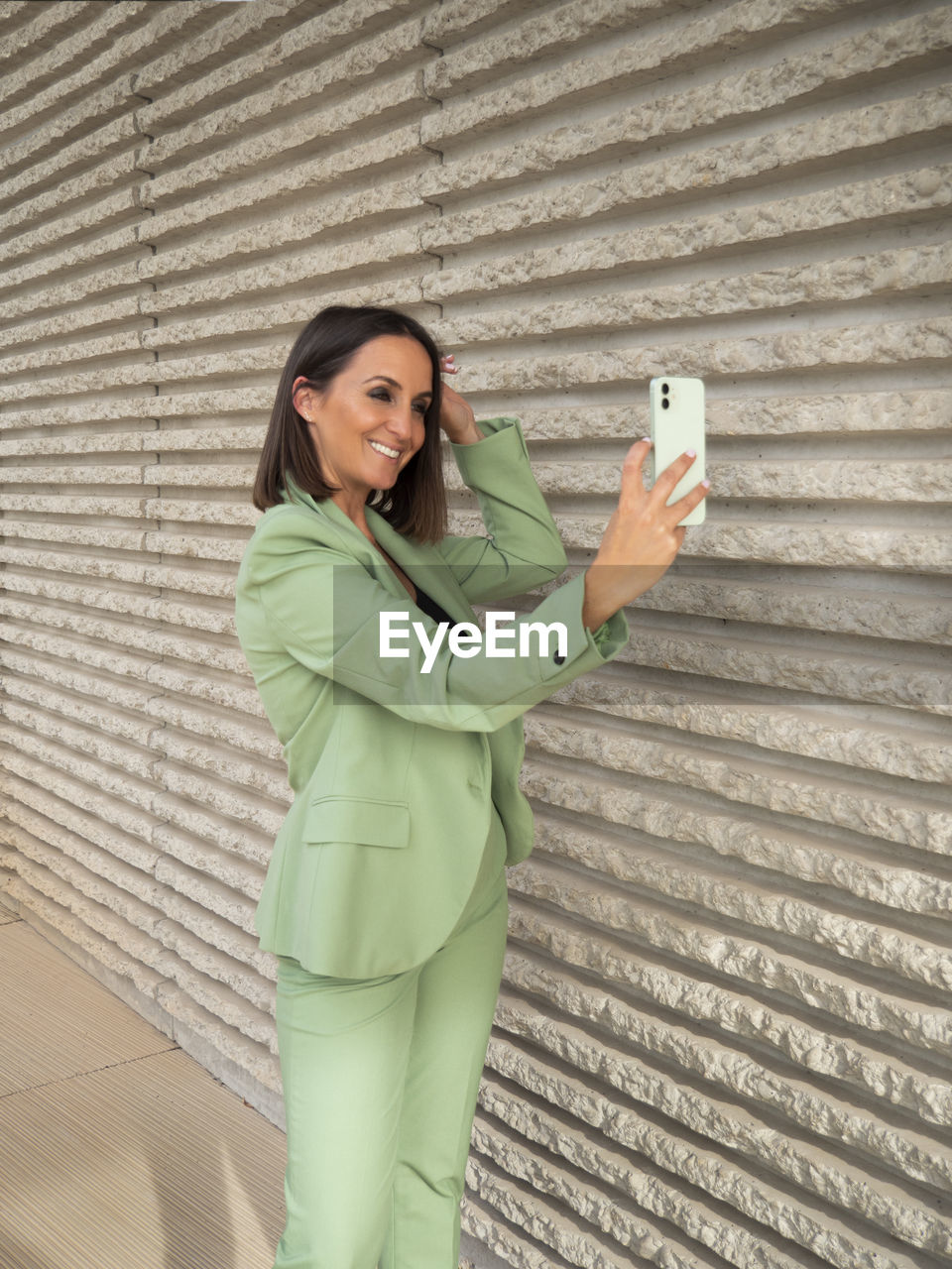 Young woman using mobile phone while standing against wall