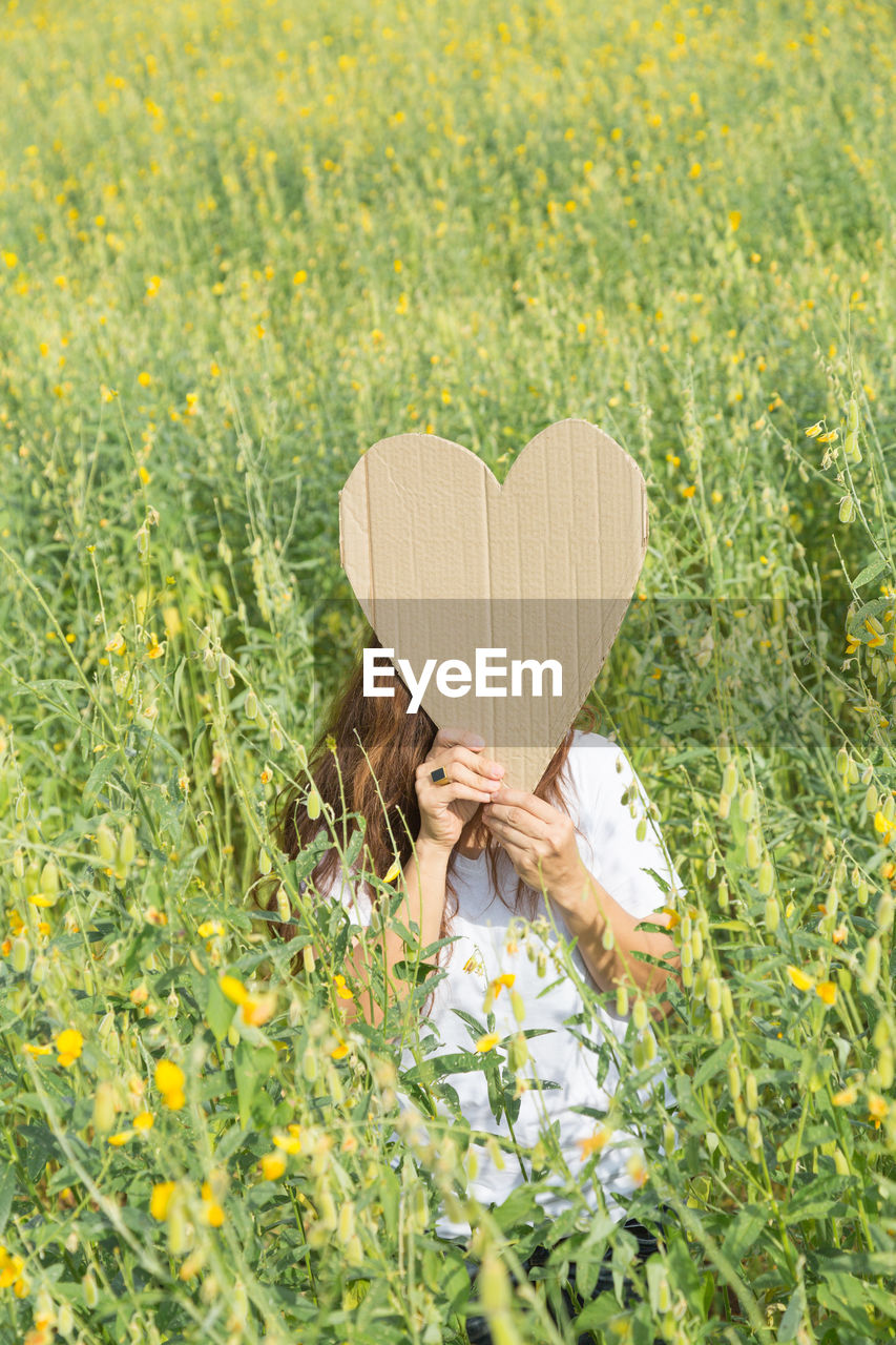 Woman with heart shape cardboard standing on field